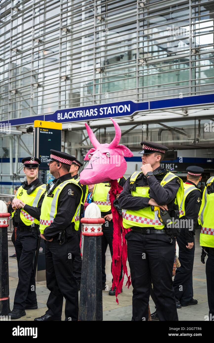 Line of police officers at the National Animal Rights March, organised by Animal Rebellion and  Extinction Rebellion and one protestor with Papier-mâché pink cow, London, England, UK. August 28 2021 Stock Photo