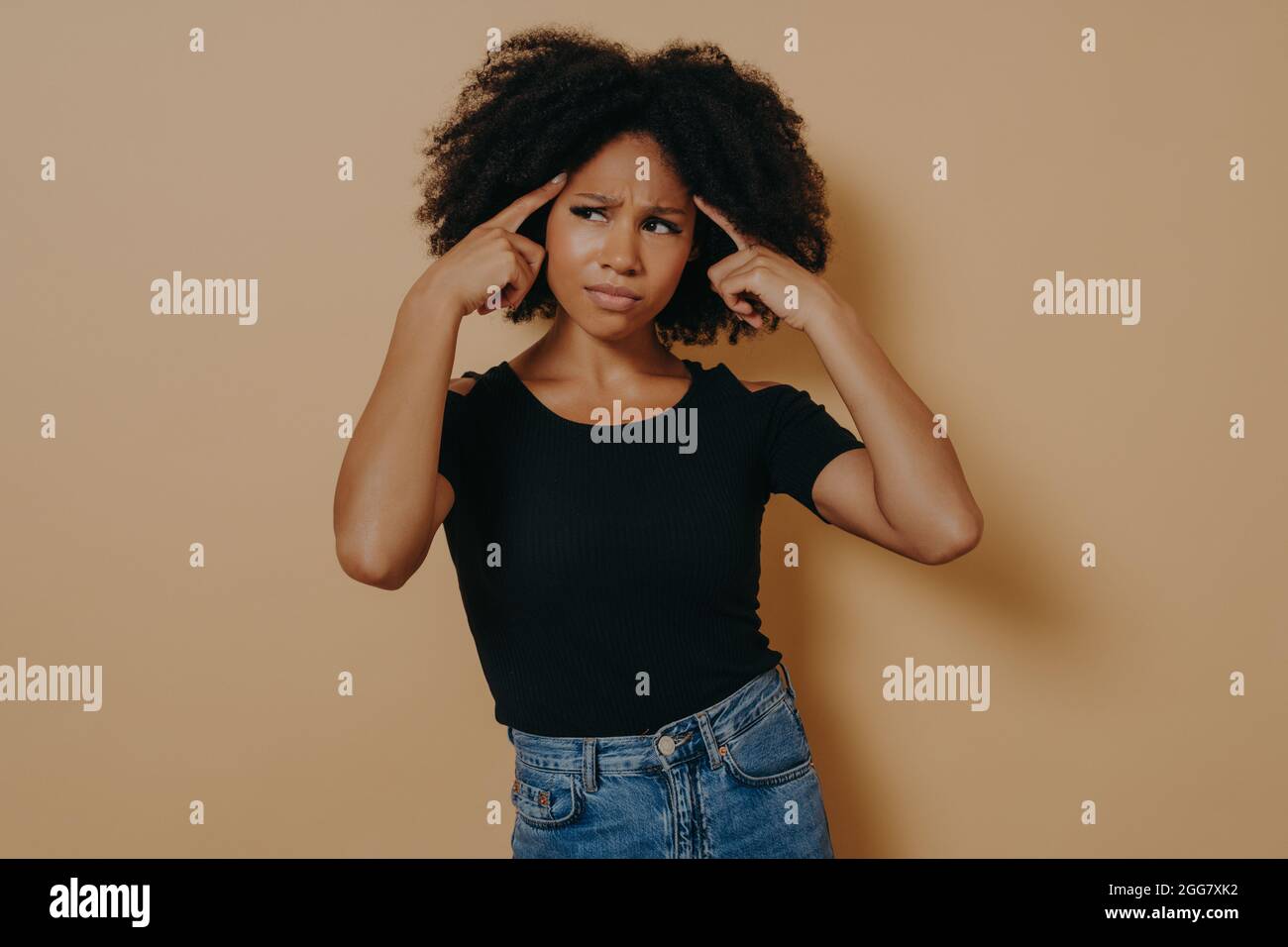 Young thoughtful mixed race woman holds fingers on temples and trying to concentrate Stock Photo