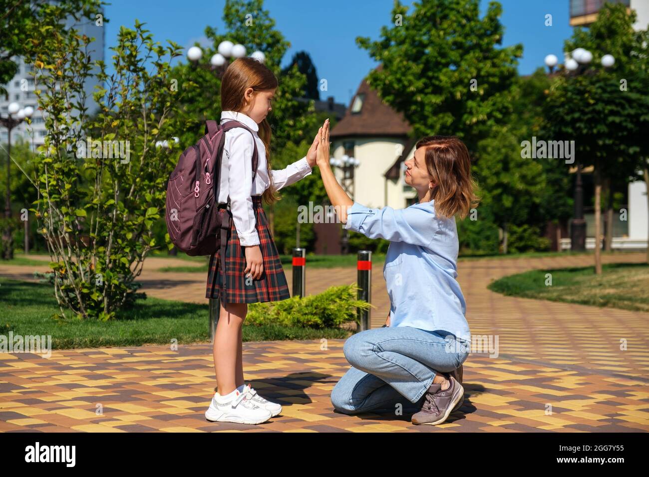 Caucasian schoolgirl with backpack and uniform says goodbye to her mother Stock Photo