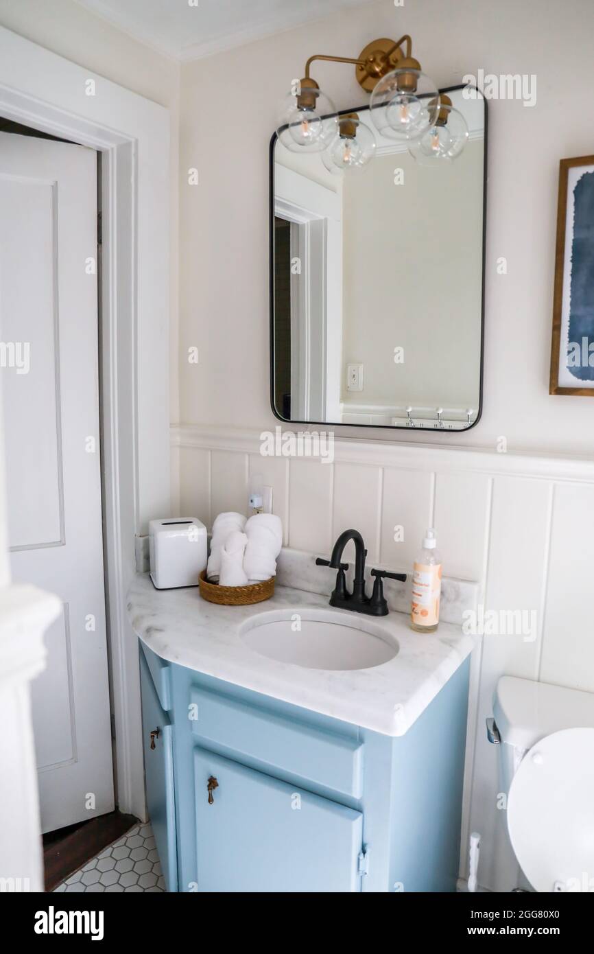 A small guest bathroom with a vintage blue vanity, retro black mirror, and clear glass light fixture in a recently renovated short term rental cottage Stock Photo