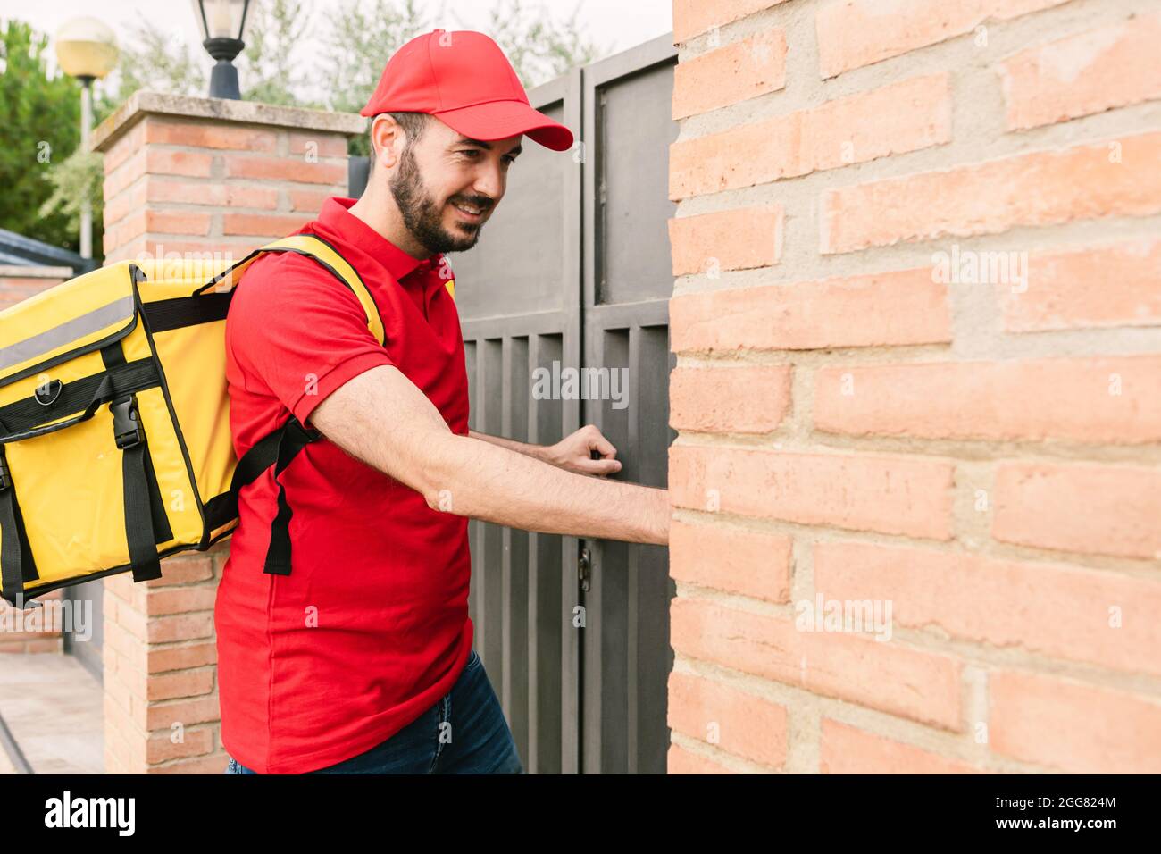 Hispanic delivery man in red uniform ringing the bell to delivery packages - Deliver service and small business concept Stock Photo