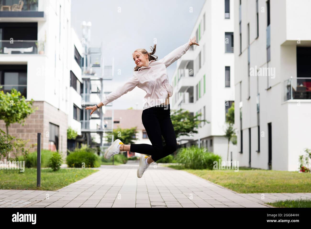 Smiling young woman jumping in modern neighborhood Stock Photo