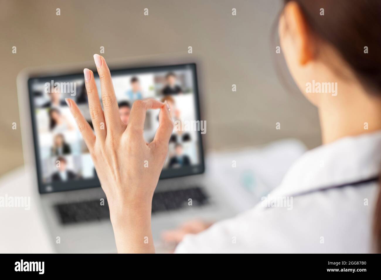 Back view of doctor making video call with laptop and showing ok gesture. Stock Photo