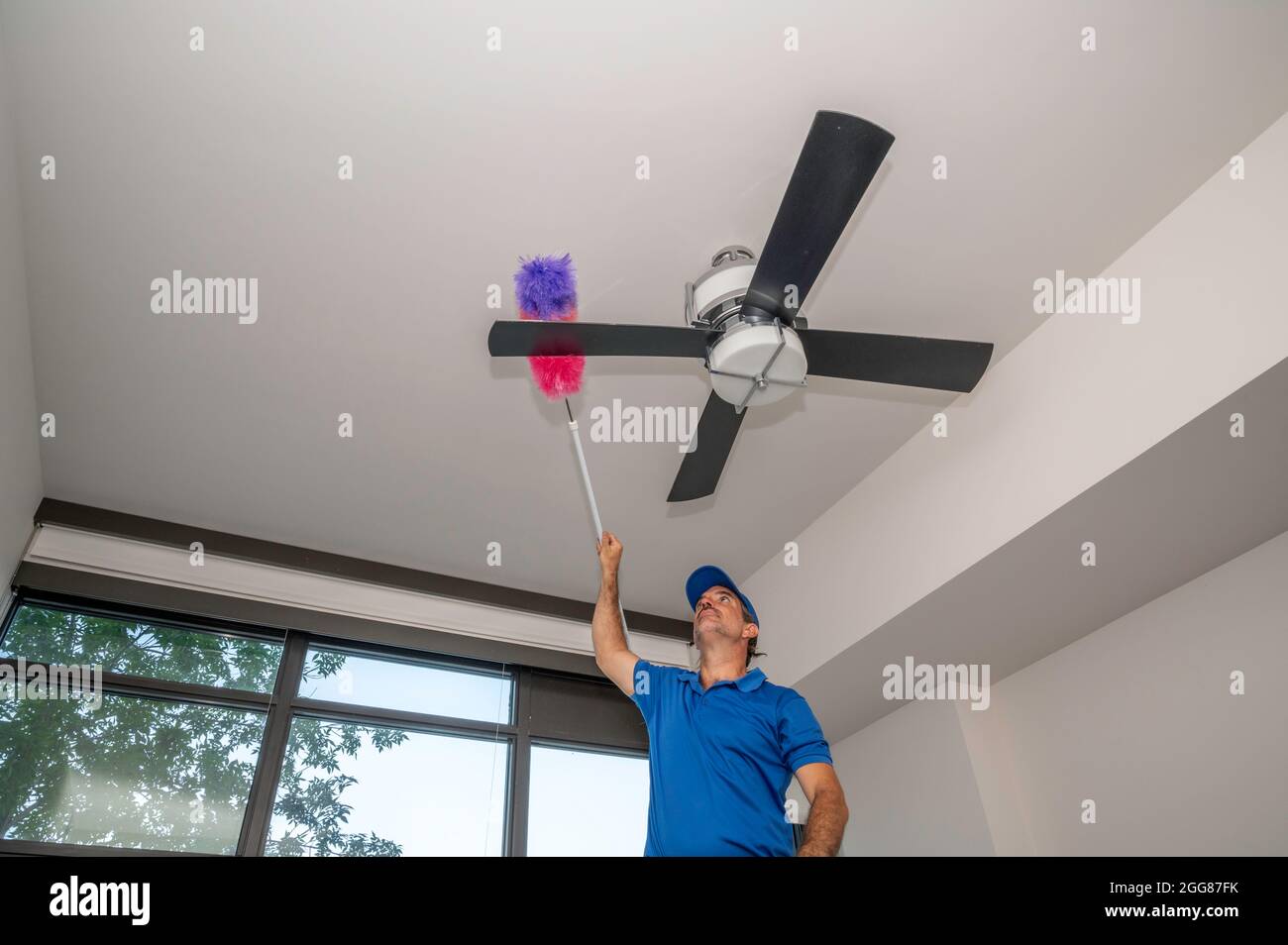 Man cleans dusty ceiling fan blades inside of a home Stock Photo Alamy