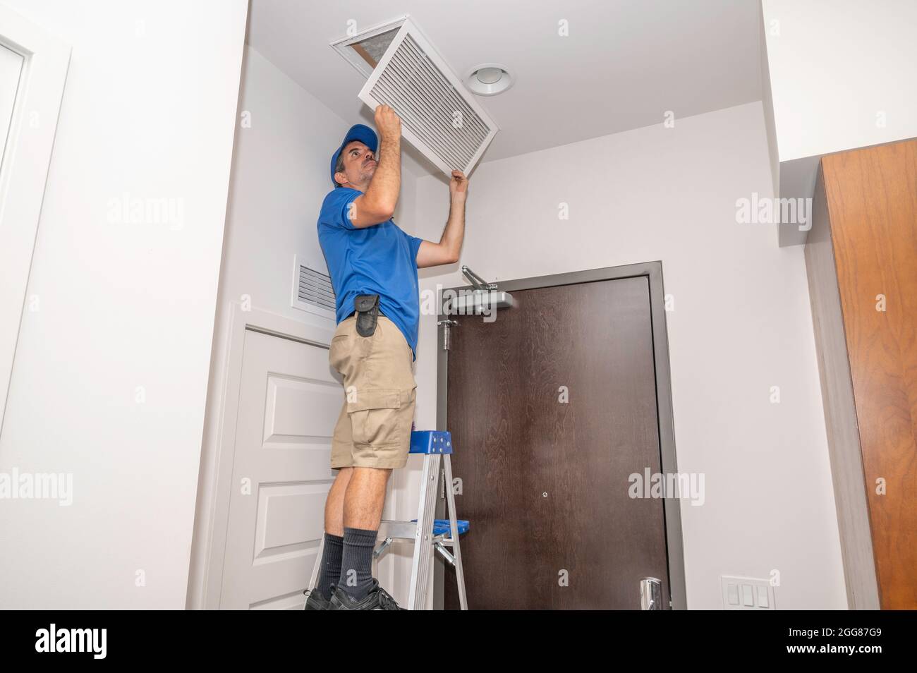 HVAC technician inspecting an air filter in a ceiling return vent Stock Photo