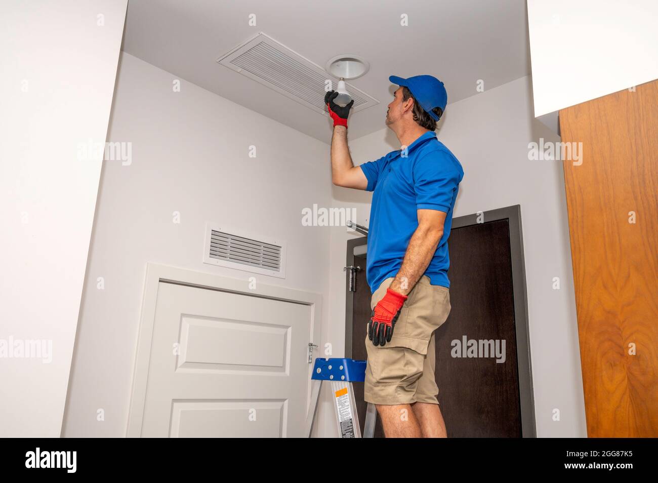 A man on a ladder changing a flood light bulb inside of a home Stock