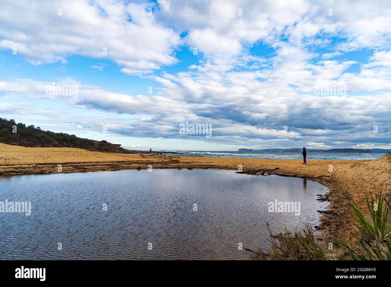 Putty Beach, Central Coast, NSW, Australia on a wild stormy day looking across the ripples of a lagoon to a solitary figure looking at the ocean Stock Photo