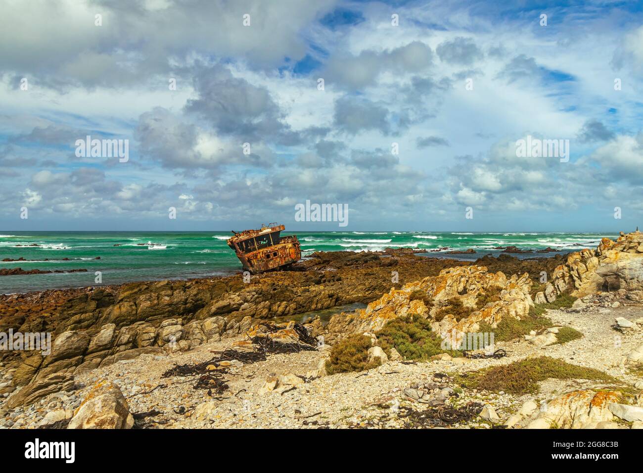 Rugged rocky shore with rusted shipwreck of Meisho Maru No.38 at Cape Agulhas in South Africa which is the southernmost point of African Continent. Stock Photo