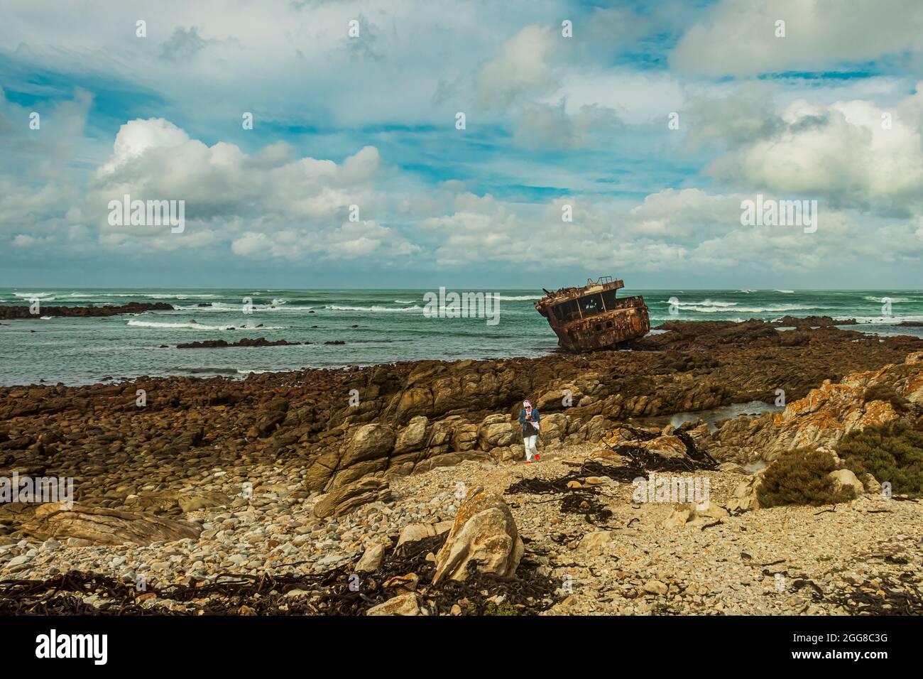 Rugged rocky shore with rusted shipwreck of Meisho Maru No.38 at Cape Agulhas in South Africa which is the southernmost point of African Continent. Stock Photo