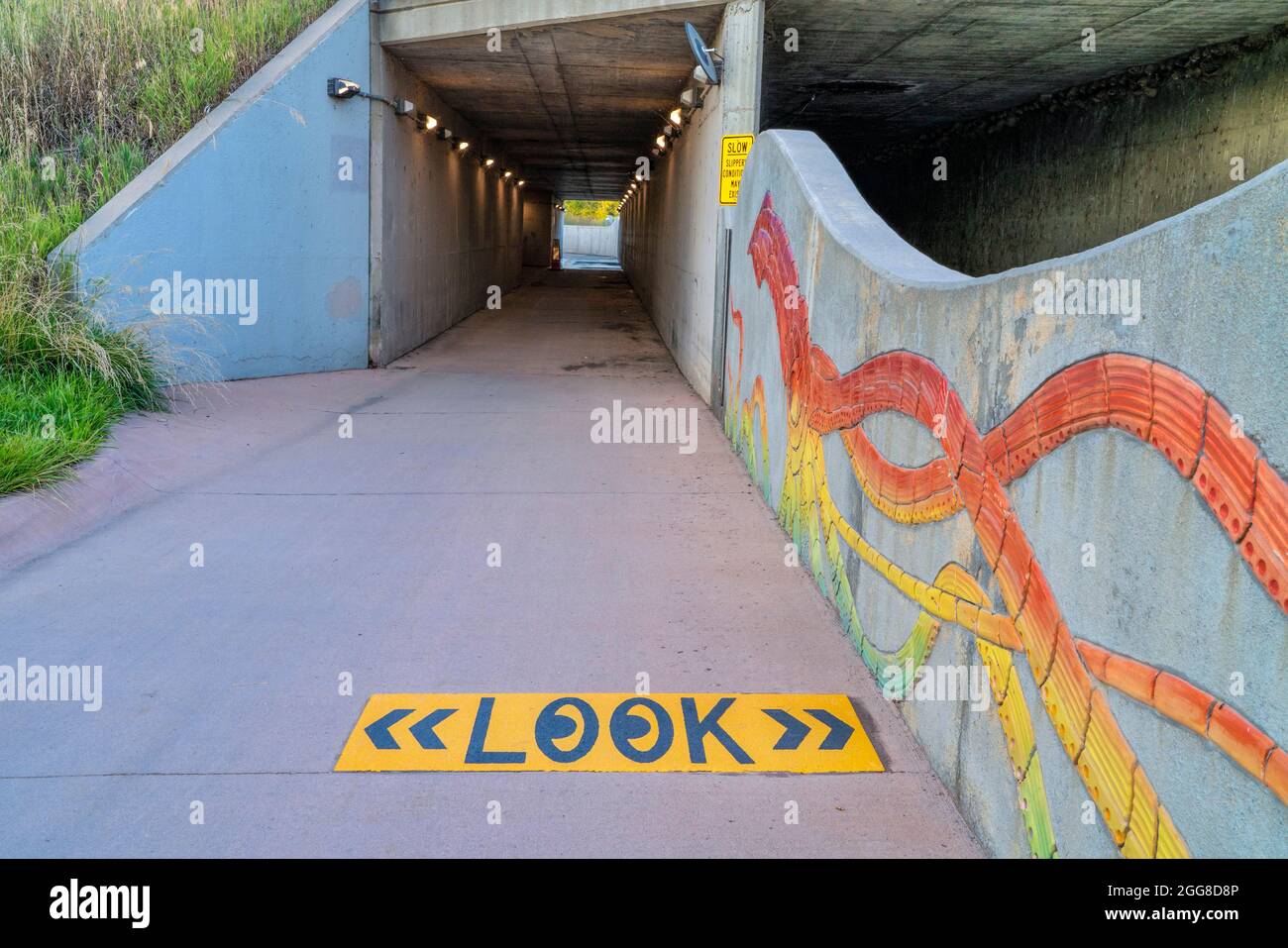 bike trail and creek go through underpass with warning sign about a risk of flooding Stock Photo