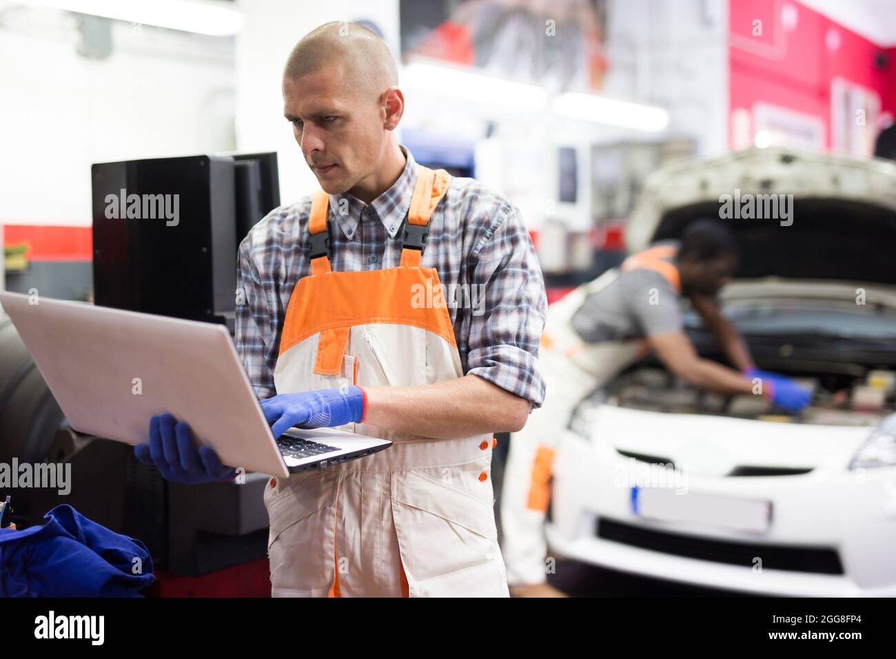 Mechanic man using laptop checking car in workshop Stock Photo