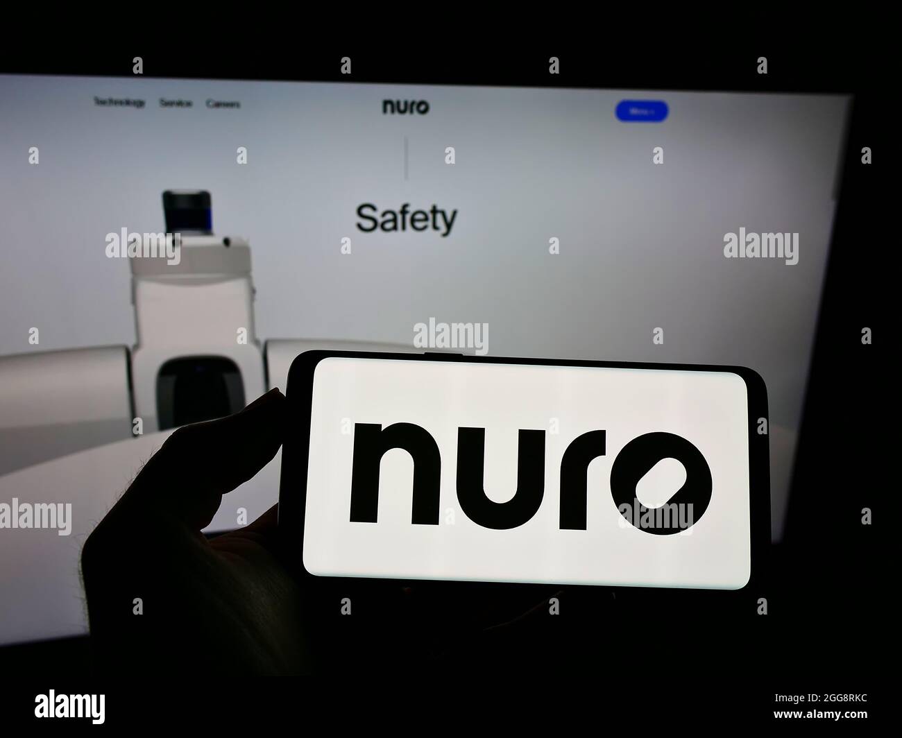 Person holding smartphone with logo of American autonomous driving company Nuro Inc. on screen in front of website. Focus on phone display. Stock Photo