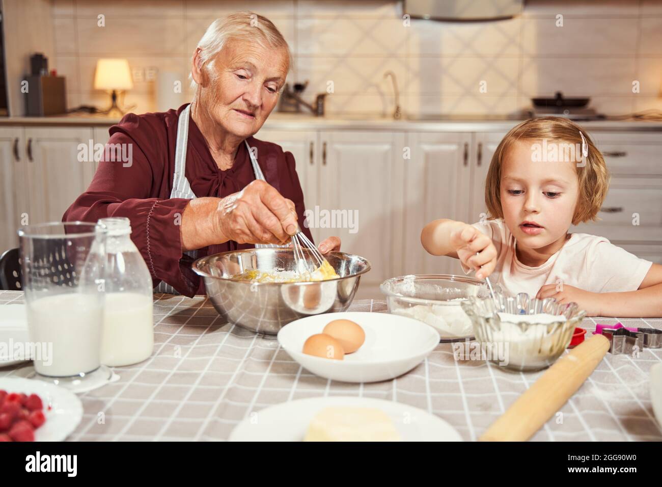 Grandmother whipping eggs with flour while girl reaching for sugar