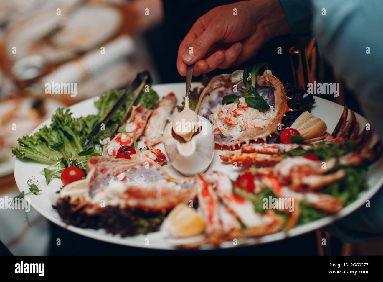 a waiter in a restaurant holds seafood dishes and serves a table catering Concept Healthy food octopus and crabs shellfish. Stock Photo