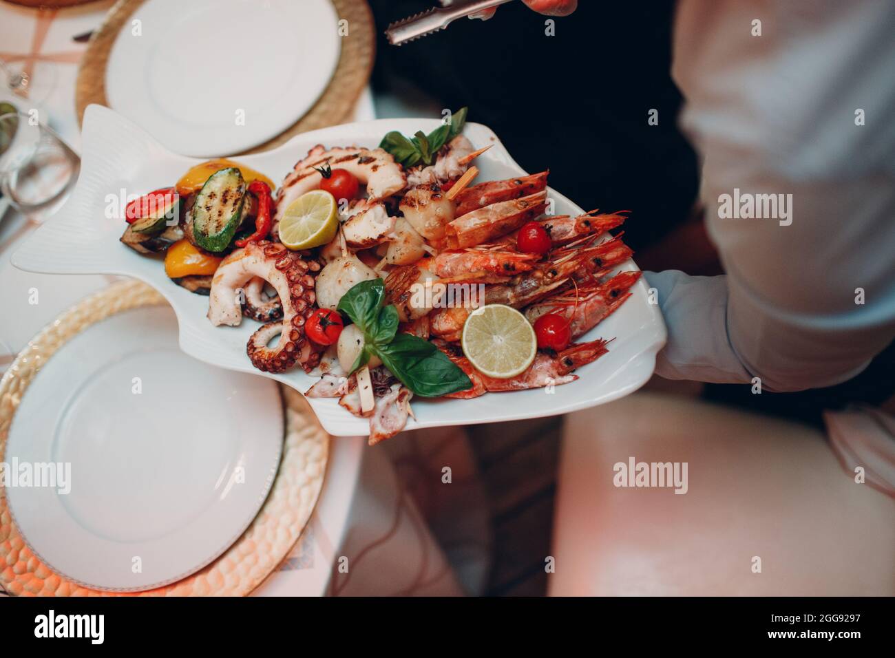 a waiter in a restaurant holds seafood dishes and serves a table catering Concept Healthy food octopus and crabs shellfish. Stock Photo