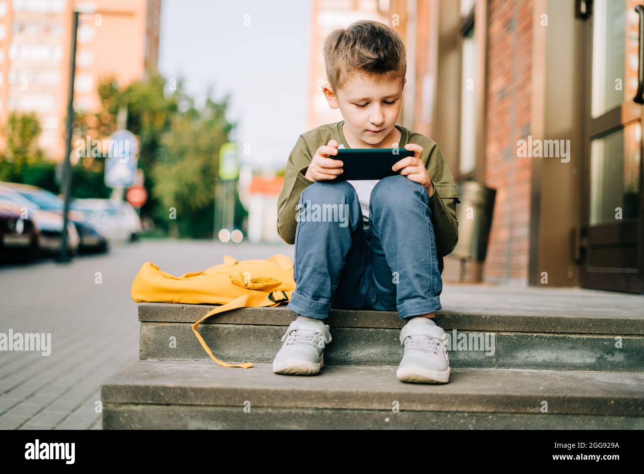 Back to school. Cute child with backpack, holding mobile phone, playing with cellphone. School boy pupil with bag. Elementary school student after Stock Photo