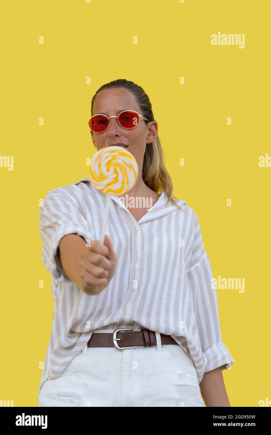 Beautiful woman in red sunglasses holding lollipop on yellow background Stock Photo