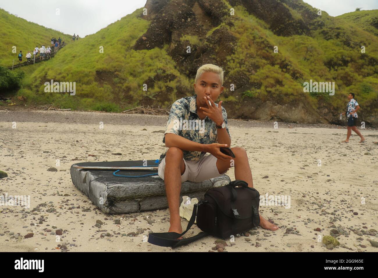 A young man sits on a board with hills on the background in Padar Island. Stock Photo