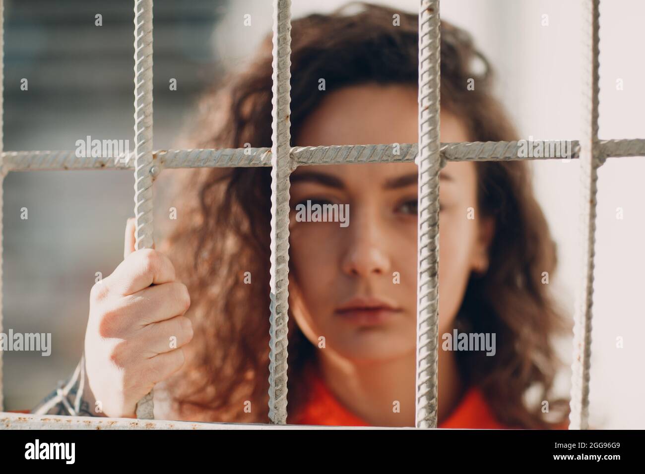 Young Brunette Curly Woman In Orange Suit Behind Jail Bars Female In Young Brunette Curly Woman In Orange Suit Behind Jail Bars Female In