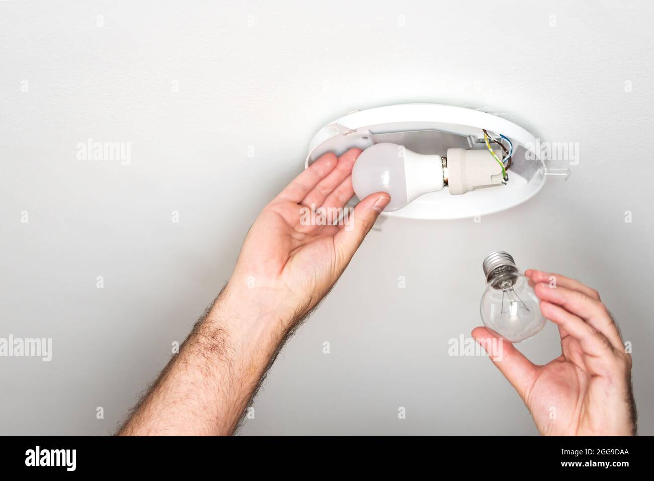 person replacing old incandescent light bulb with energy saving LED bulb in ceiling light, power saving concept Stock Photo