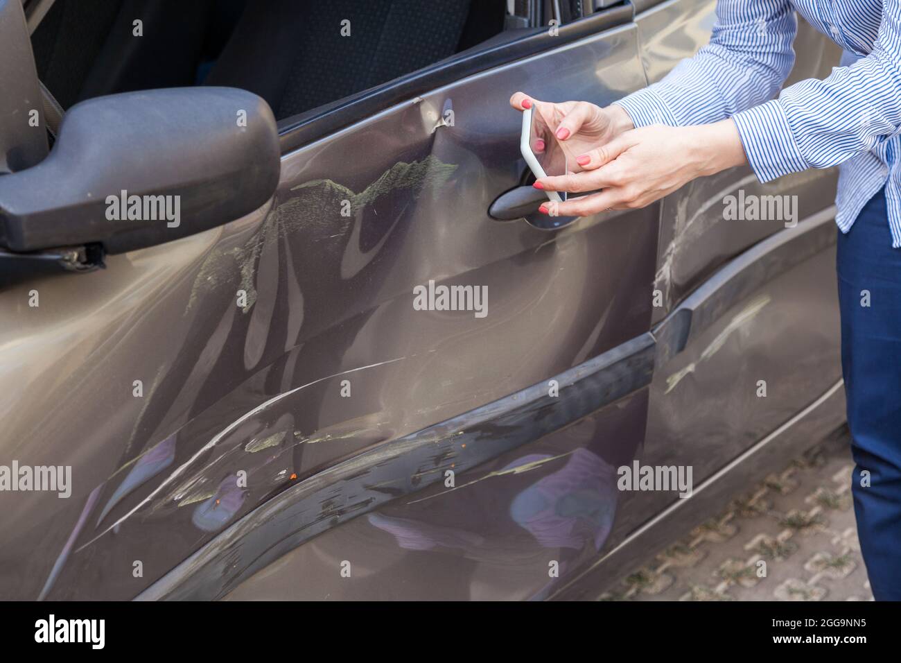 Faceless portrait of woman hands holding smartphone and taking photo of dents and scratches on door of crashed automobile after road accident, picture Stock Photo