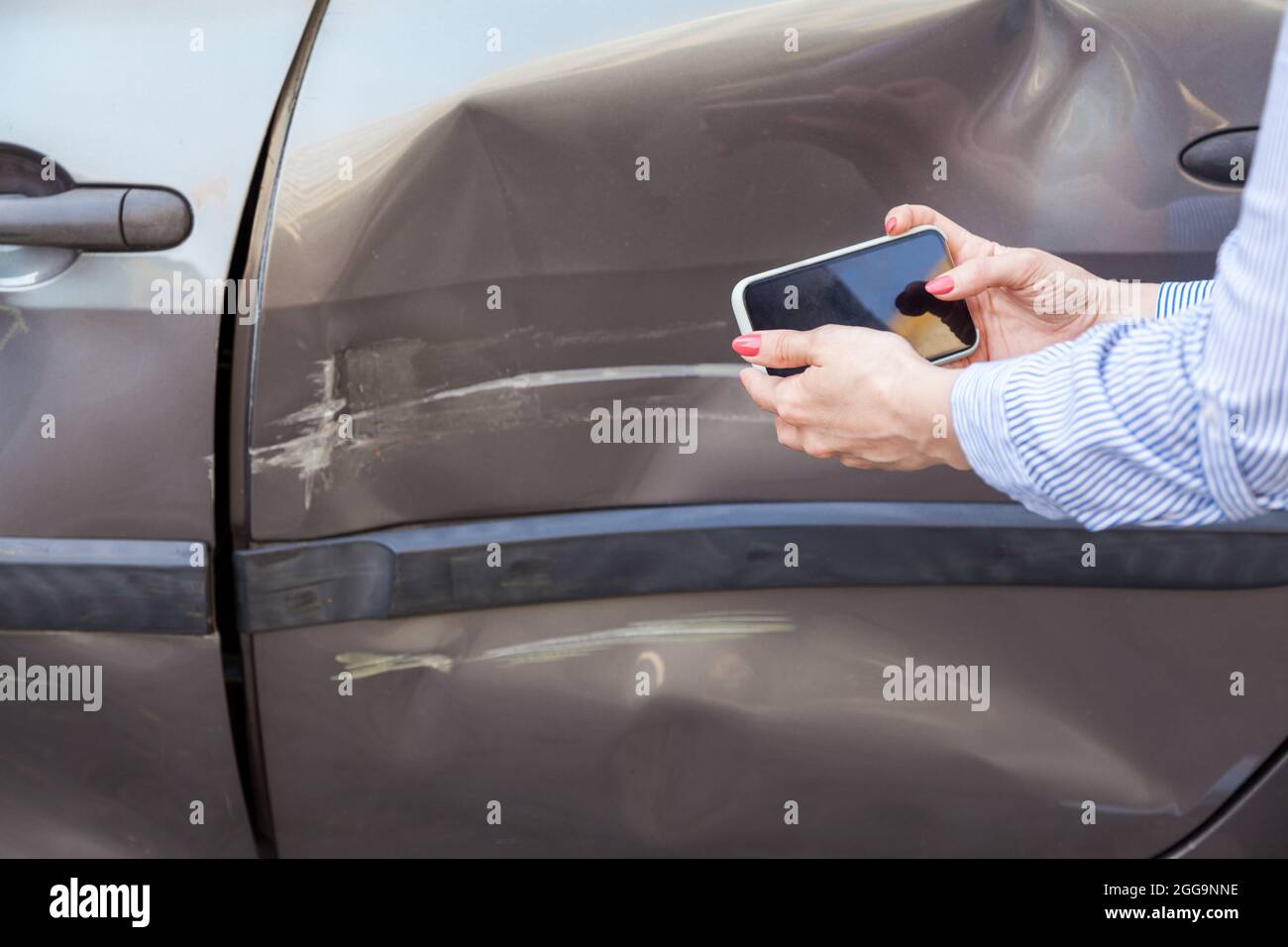 Unknown woman with mobile phone in hands taking picture of damaged part of car, photographing scratches and dents on auto door, records the consequenc Stock Photo
