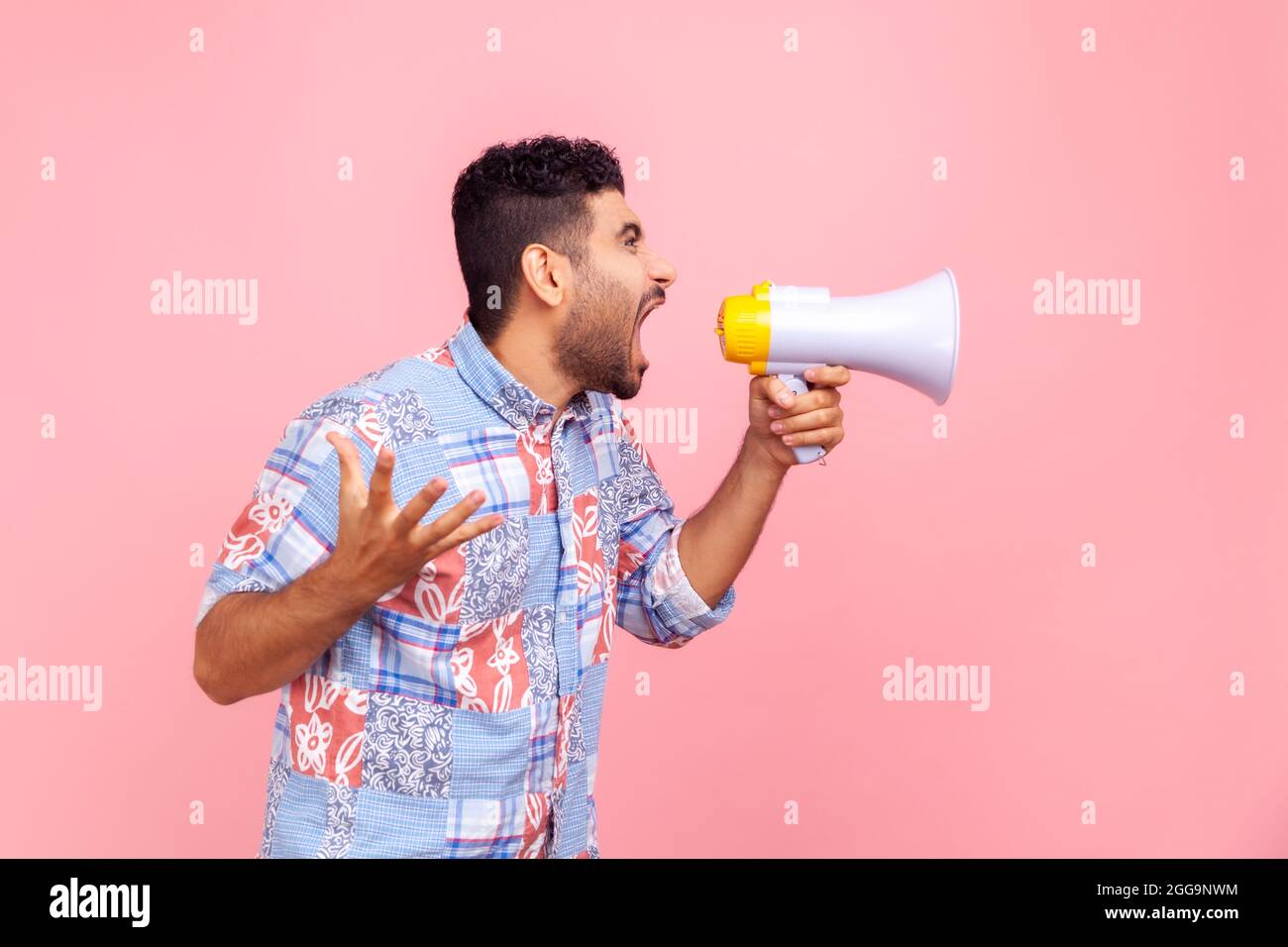Profile portrait of nervous bearded man in blue casual style shirt loudly speaking screaming holding megaphone, announcing important message. Indoor s Stock Photo
