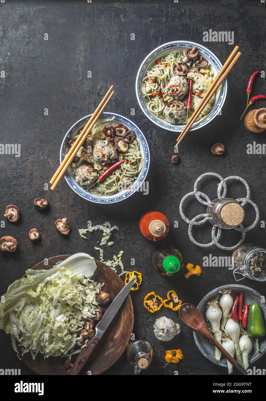 Asian food. Bowls with noodles and Shiitake mushrooms, chili pepper , chopsticks and meatballs on dark rustic background with fresh Asian cuisine ingr Stock Photo