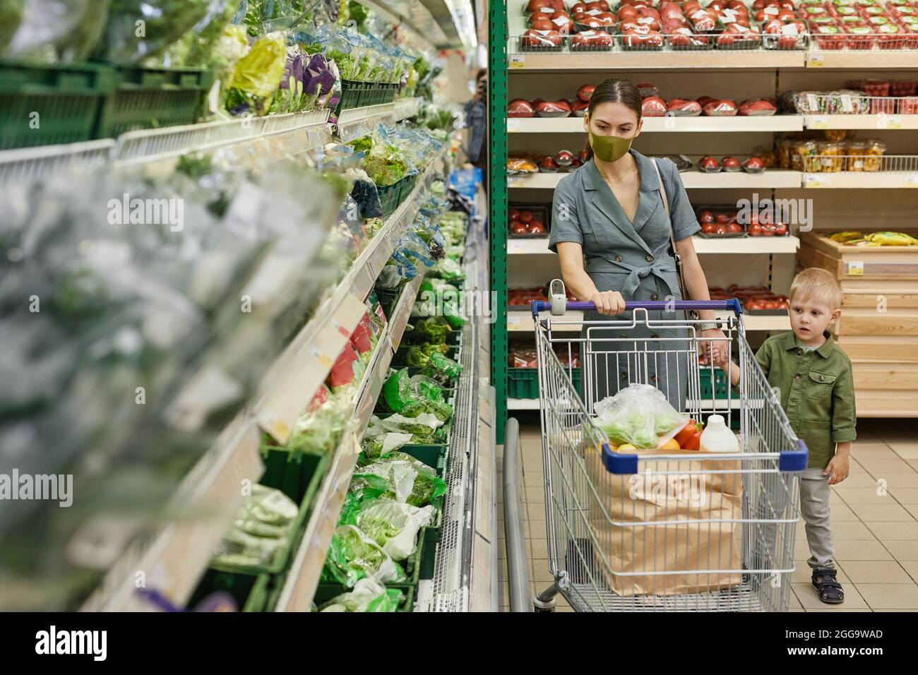 Pregnant young Caucasain woman in cloth mask pushing shopping cart and