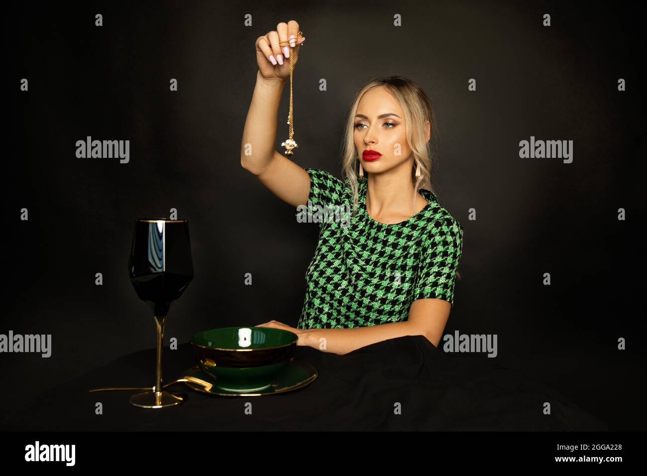 Beautiful young witch woman with red lipstick on her lips and makeup conjures on black background, magic ritual for wealth. Stock Photo