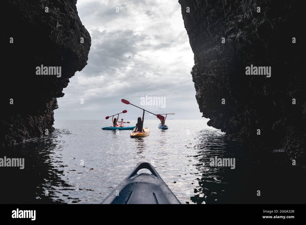 Group of happy kayakers are walking or training with instructor at sea bay between two big rocks. Sea vacations concept Stock Photo