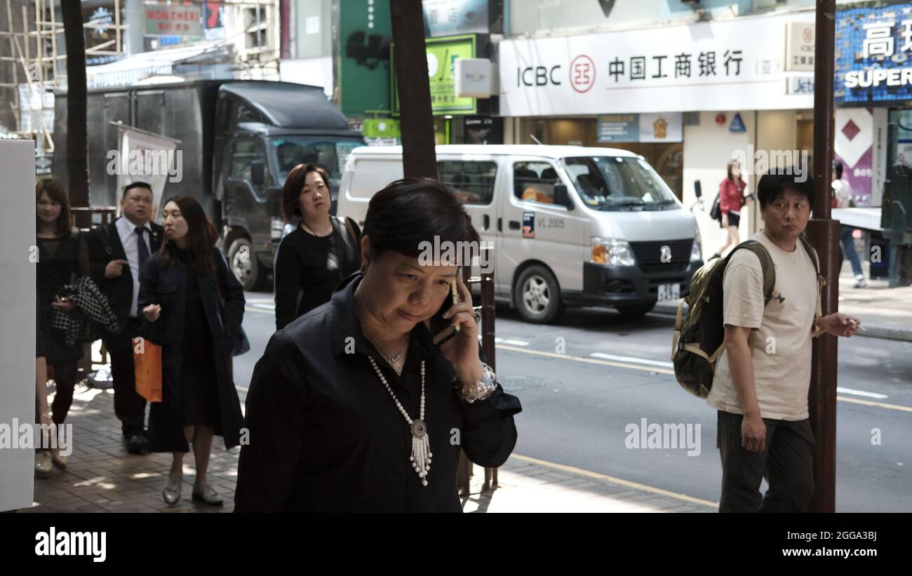 Chinese Lady Walking Talking on Mobile Phone Neighborhood Street Scene Tsim Sha Tsui, Kowloon, Hong Kong, ChinaC Stock Photo