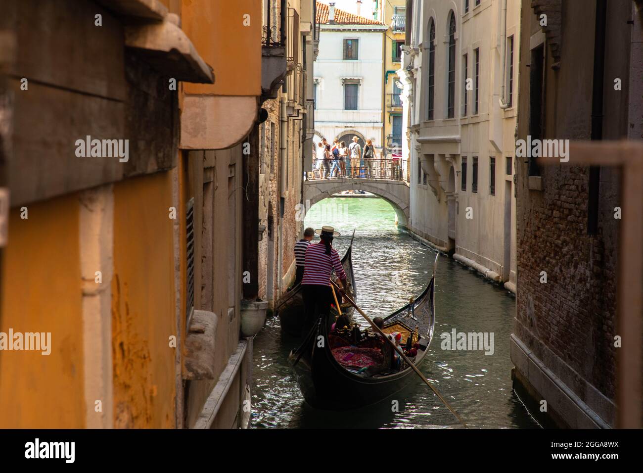Gondola and gondolier in Venice on the water canal with tourists on the bridge Stock Photo