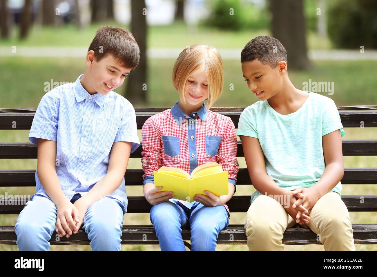 Cute kids reading book on bench Stock Photo