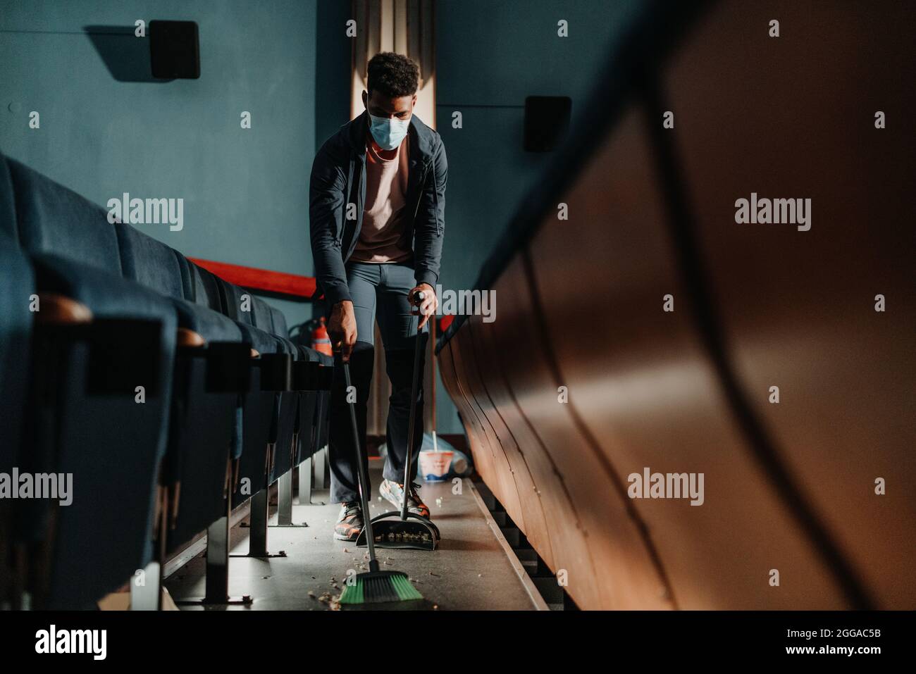 Young man cleaner sweeping floor in the cinema after the film, coronavirus concept. Stock Photo