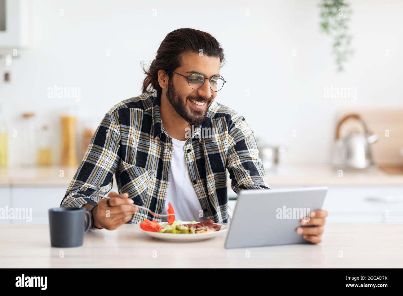Handsome arab guy having breakfast, using digital tablet, copy space Stock Photo