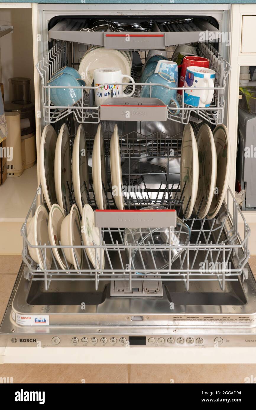 A fitted dishwasher full of clean washed dishes, mugs and crockery in a domestic kitchen at home UK, Britain Stock Photo