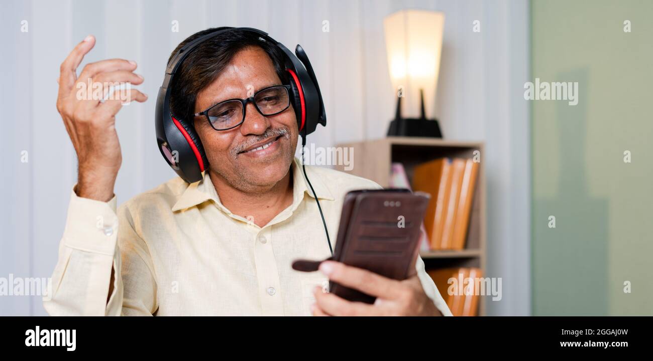 Happy smiling businessman enjoying by listening music in headphones at office - concept of taking break, relaxation while at work Stock Photo