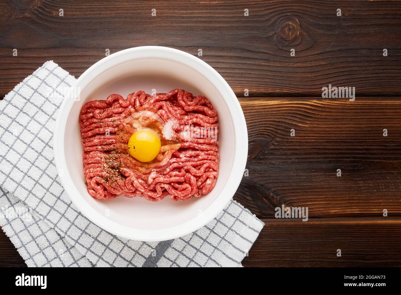 Raw ground beef or minced beef in a white bowl on wooden background. Top view, copy space for text Stock Photo