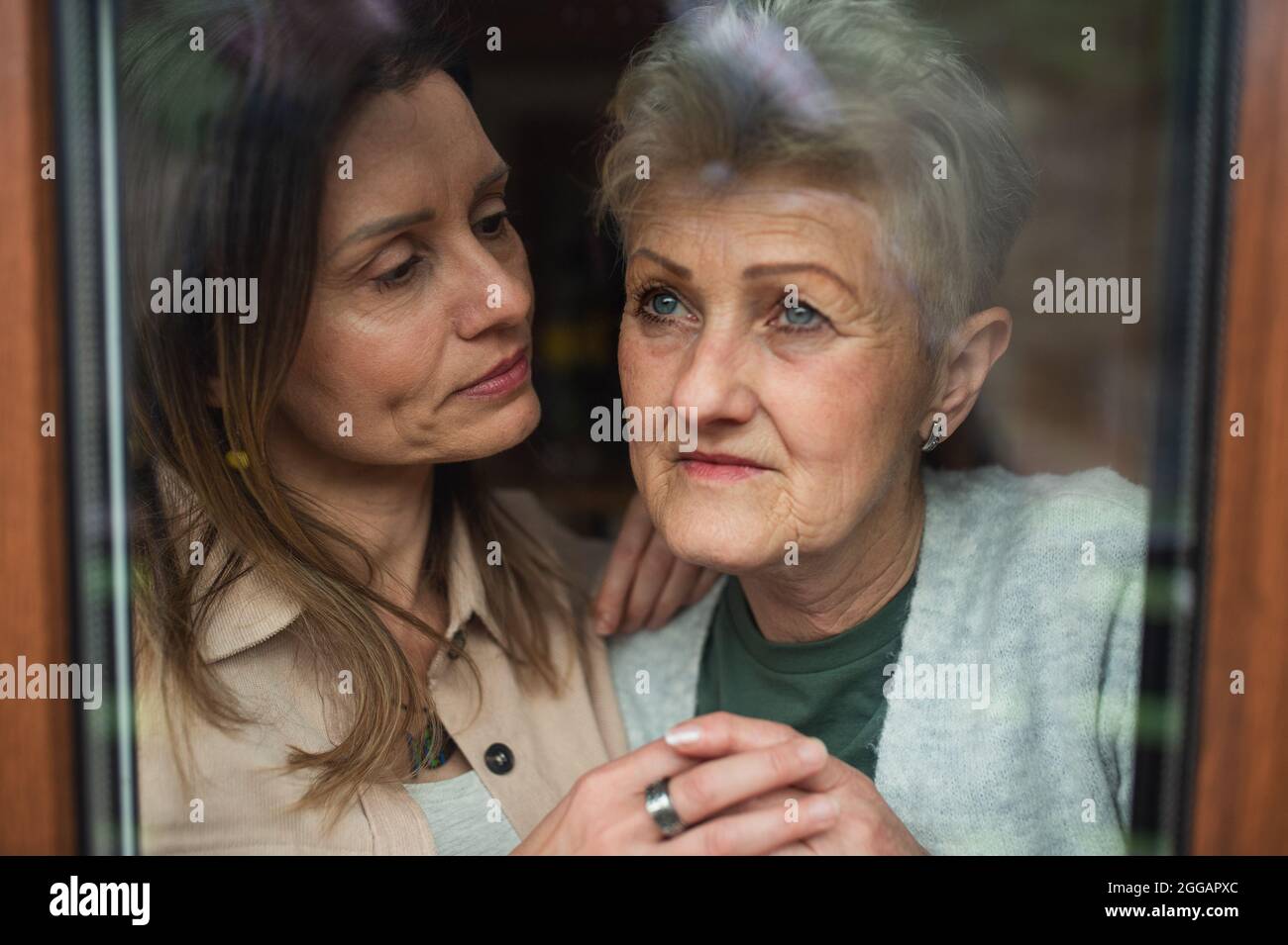 Close-up portrait of sad senior mother with adult daughter indoors at home, hugging. Stock Photo