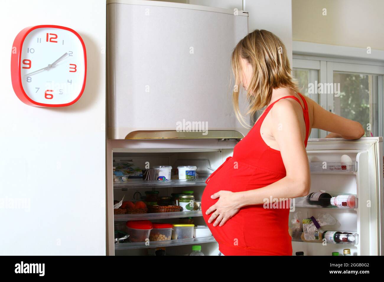 Craving pregnant woman looks for food in the fridge Stock Photo