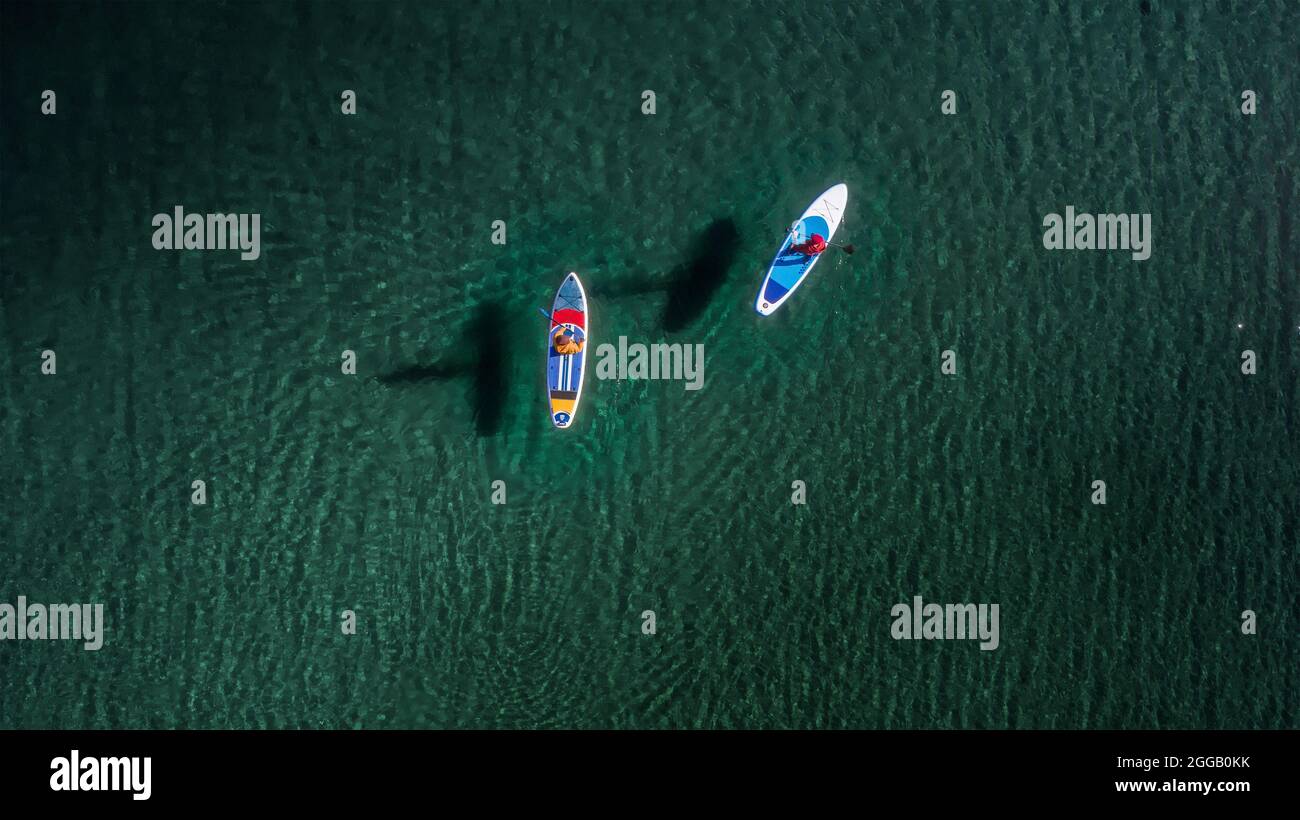 Two sporty peoples are walking on sup boards with paddles at turquoise water. Aerial drone view Stock Photo