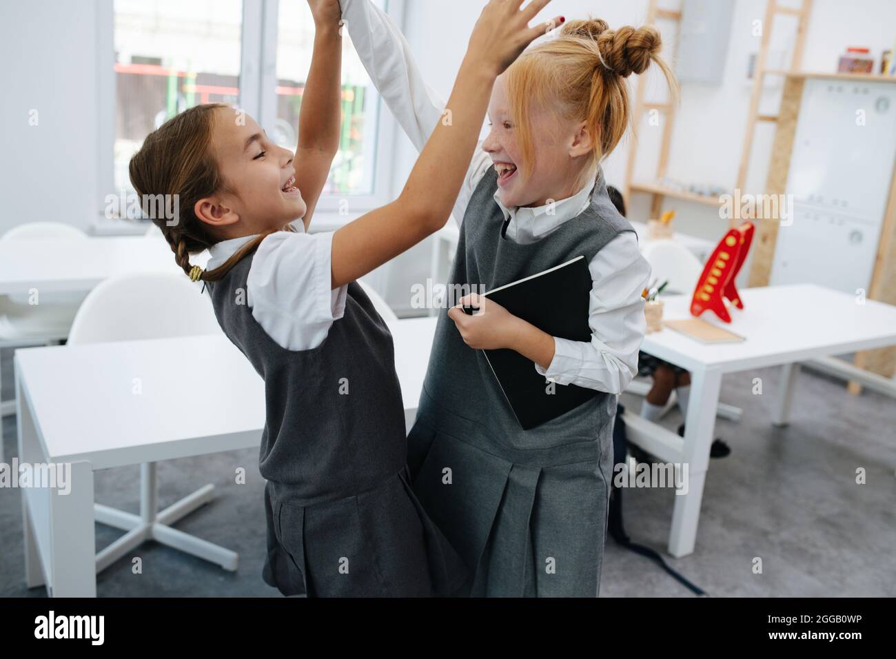 Two elementary schoolgirls having a friendly fight in a school. In a bright schoolroom. Stock Photo