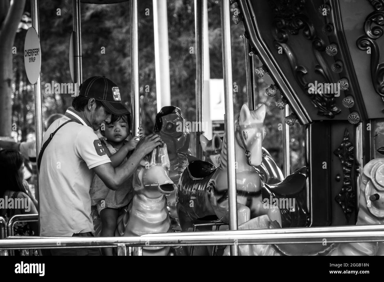 SUBIC, PHILIPPINES - Aug 09, 2017: A grayscale of a father caring for his daughter at a carousel of Subic Bay in Olongapo City, Zambales, Philippines Stock Photo