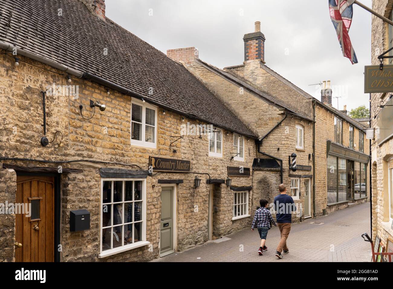 A man and a boy walking down Church Street in Stow on the Wold surrounded by traditional Cotswold Limestone buildings. Gloucestershire, UK Stock Photo