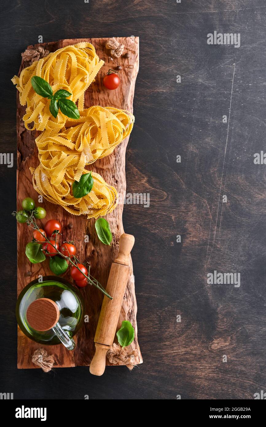 https://c8.alamy.com/comp/2GGB29A/tagliatelle-homemade-pasta-basil-leaves-flour-pepper-olive-oil-cherry-tomato-and-rolling-pin-and-pasta-knife-on-dark-old-wooden-background-food-2GGB29A.jpg