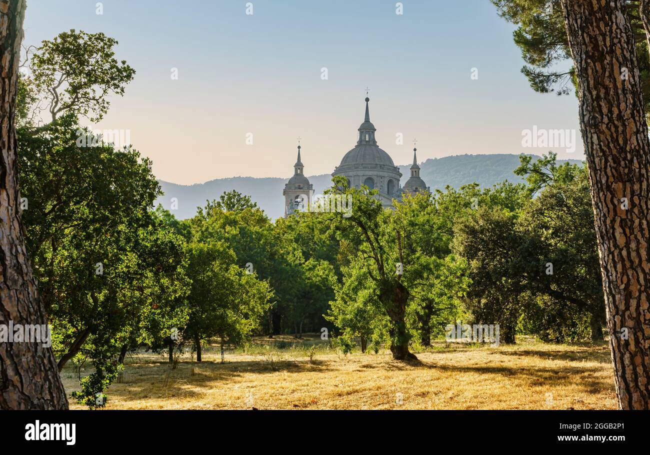 Sunset view of the dome and towers of the San Lorenzo de el Escorial monastery from a forest in early autumn and the mountains in the background. Stock Photo