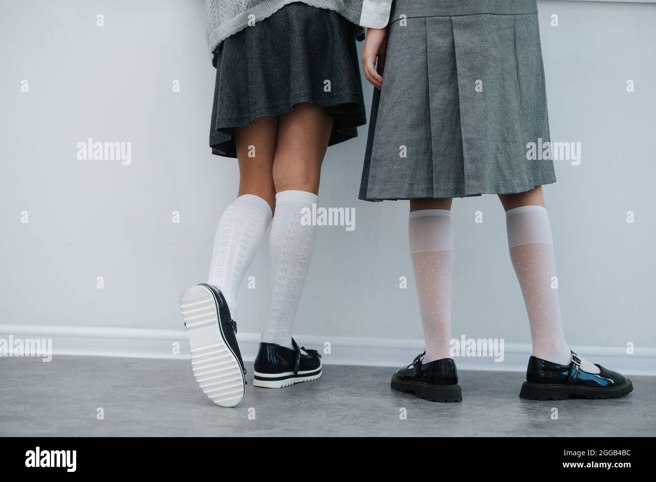 Legs of two schoolgirls stadning next to a wall close to one another. Both wearing skirts and knee-high socks. Stock Photo