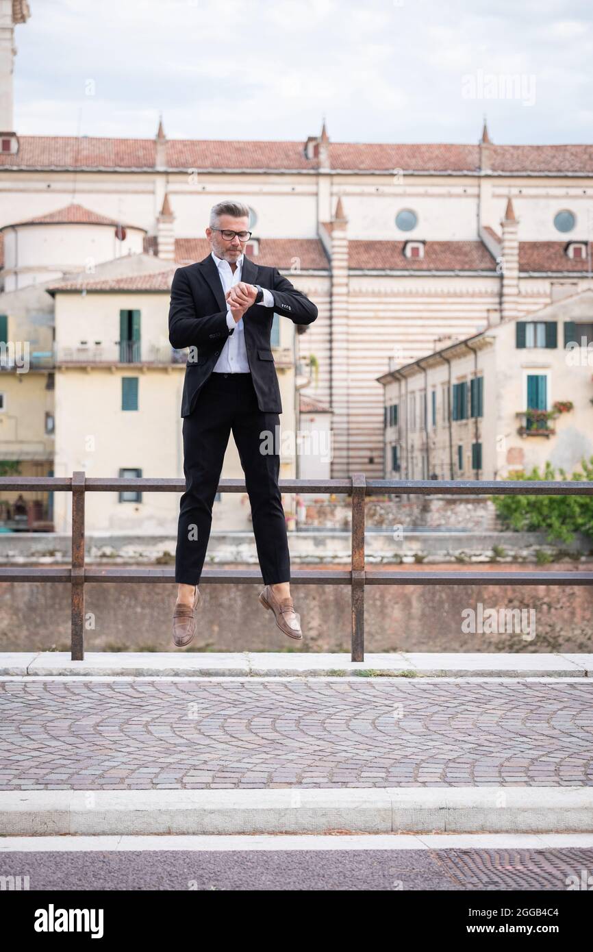 Handsome businessman checking the time on his watch and jumping from stationary. Strange and surreal situation Stock Photo