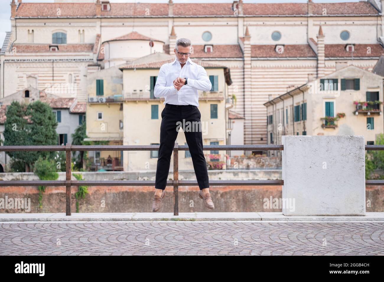 Handsome businessman checking the time on his watch and jumping from stationary. Strange and surreal situation Stock Photo